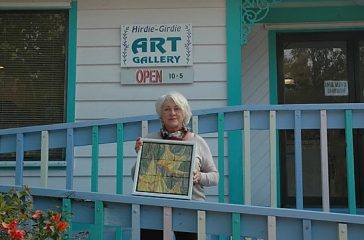 Sue Housler standing in front of the Hirdie Girdie Gallery holding one of her works of art